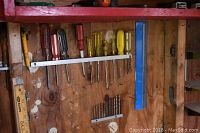 Photo showing variety of screwdrivers, drill bits arranged on wood panel