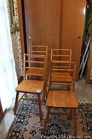 Four wooden ladder back chairs arranged in the corner of a room, showing natural wood finish and signs of wear.