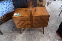 Closed wooden sewing basket with rectangular shape, wooden handle, and four legs on tiled floor.