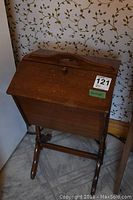 Front view of vintage wooden sewing box on stand, closed with hinged top lid and curved legs.
