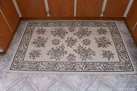 Full view of machine made floral area rug on tiled floor showing pattern and border.