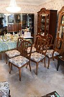 Six chairs arranged in room showing carved backs and needlepoint seats.