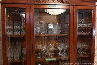 Left and center sections of wooden glass cabinet with assorted crystal and glassware in varying sizes and stem styles.