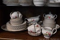 Full view of stacked plates, tea cups piled on top, cream pitcher, sugar bowl and serving platter showing pattern and condition.