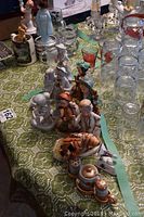 Assortment of approximately 10 figurines on a green lace tablecloth including Goebel figures and various glassware around.