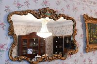 Full frontal view of mirror hanging on floral wallpapered wall showing entire frame and reflective surface.
