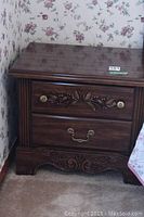 Front view of one night stand showing carved floral decoration, brass hardware, and dark wood finish.