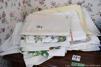 Stack of assorted folded tablecloths and runners in white, cream, and floral prints placed on wooden surface.