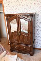Front view of the wood frame armoire showing mirrored diamond-patterned glass doors and lower faux wood drawer with metal handles.