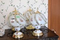 Four vintage table lamps arranged to show matching pairs, porcelain bases with floral design, stained glass floral shades with brass frames and finials.