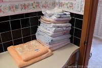 Stack of approximately 14 assorted towels in various colors and sizes, showing wear.