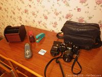 Photo showing Minolta camera on wooden table next to camera bag, stapler, remote, and wooden desk organizer