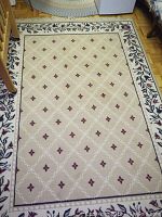Full view of the machine made area rug showing beige center with diamond lattice pattern and small red floral motifs