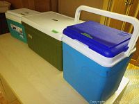 Photo showing three coolers on a table: Coleman (olive green/white), Flair (teal/white), Thermos 1500 (blue/white with purple lid)