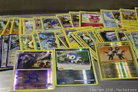 Array of various Pokemon trading cards laid out in rows including holographic foil cards at the front.