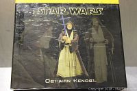 Box shows Star Wars logo, image of the Obi-Wan Kenobi metal figurine, Obi-Wan Kenobi name, some wear and smoke damage visible on the box surface.