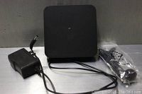 Black square MQX Pro 4K Android TV box alongside power adapter and antenna cord on grey surface.
