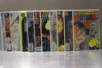 Front-facing image showing 12 assorted comics upright in protective sleeves, with visible titles including Batman, Superman, Flash, and Detective Comics.