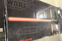 Box front showing Star Wars The Black Series branding with an image of the Kylo Ren cross guard lightsaber emitting red light, box is visibly dented and creased.