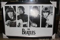 Full view of the framed Beatles poster with four black and white portraits and the band name at the bottom. Protective corner guards are on the frame.