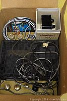 Photo showing an old device with a gold control panel, power switch, and tangled cables alongside a Rolleiflex 35F camera accessory in its original box and some wiring.