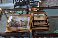 Top view of seven framed art pieces stacked on a table showing various sizes and frame styles.
