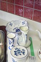 Five ceramic pieces on white countertop near sink: pedestal bowl, jug, small vase, lidded jar, and floral teapot with cup and saucer. Blue and white hand-painted designs apparent.