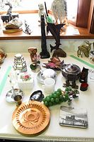 Photo of wood carvings, bowls, decorative fruit, metal pot, various figurines and key holder on a white tabletop, showing the variety and condition of items.