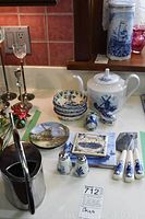 Full display of items including Delft teapot, stacked small bowls, salt & pepper shakers, trinket box, decorative plates, and cheese knives on a white surface