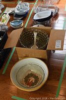 Top view of box containing large textured glass punch bowl with white ladle and background of assorted glass dishes.