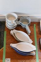 Stack of small white ceramic dishes with handles, gray handled dish, and small oval white plates.