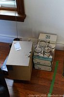 Photo showing boxed sets of Cristal d'Arques whiskey glasses stacked with loose glassware adjacent