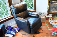 Black leather electric recliner chair positioned near window with visible power cord and remote control on the side.