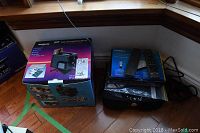 Wide view showing Argus Co-Producer IV box next to Zinwell converter box with remotes and cables on wooden floor.
