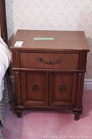 Front view of one night table showing drawer and cabinet doors with metal handles and carved legs.