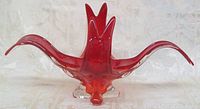 Front view of red glass amoeba bowl showing its flowing, organic shape with three upward and outward curved points and clear glass base with four feet.