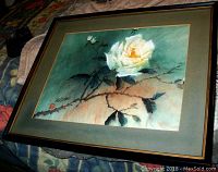Framed oil painting showing white-yellow rose on thorny branch with leaves and background in green and peach hues.