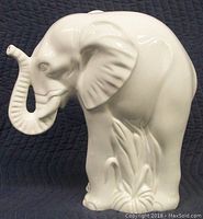 Front side view of a white glazed porcelain elephant statue on a black quilted background.