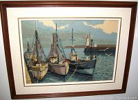 Frontal view of the embroidered artwork depicting boats in a harbor with a wooden frame and glass