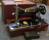 Front angle view of the Monarch sewing machine in its open carrying case showing black and gold detailing, foot pedal, and case condition.