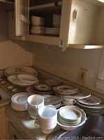Photo showing multiple stacked plates, bowls, and teacups of varying sizes with floral patterns on kitchen counter and inside a cabinet.