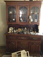 Front view of the entire china cabinet showing glass door hutch with shelves, top with displayed decorative items, and base with drawers and cabinet doors.