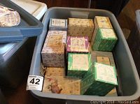 Plastic bin filled with more than 20 boxed Enesco Precious Moments figurines showing various colorful patterned boxes.