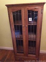 Full view of the wooden cabinet with closed leaded glass doors and visible knobs, placed against a wall.