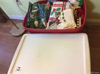 Top view of vinyl tablecloths and holiday-themed fabric dishcloths in a red plastic bin.