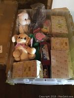 Plastic bin filled with boxed Precious Moments figurines and various stuffed animals including a tan dog plush.