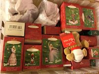 Plastic bin filled with Hallmark Keepsake Ornaments in original boxes, stacked showing various designs including Barbie Barbie Victorian series and Dr. Seuss ornaments. Also visible a plush Baby Ninjy dog with a tag.