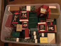 Wide shot of the plastic bin filled with approximately 30 boxed Hallmark Keepsake Ornaments in assorted packaging.
