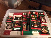 Plastic bin filled with multiple Hallmark Keepsake Ornaments in green boxes with red ribbons stacked inside.