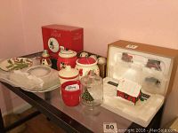 Photo showing a variety of holiday items including ceramic plates, cookie jars, cups, and a Christmas village house in packaging.